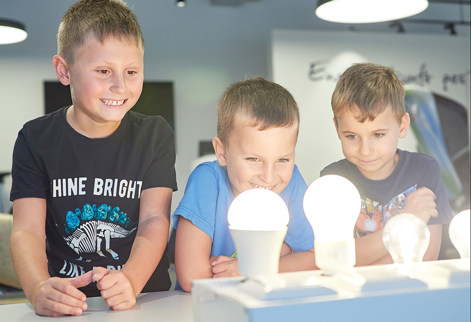 Drei Kindergartenkinder betrachten leuchtende Glühbirnen