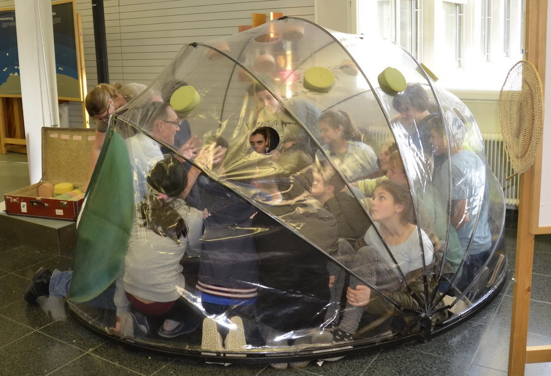 Kinder und Lehrer sitzen in einem runden Treibhaus
