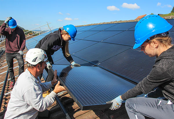 Schülerinnen installieren Solarpanels auf einem Dach